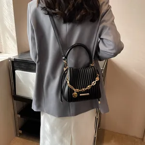 Détail du sac seau plissé noir avec chaîne dorée épaisse et breloque logo ronde