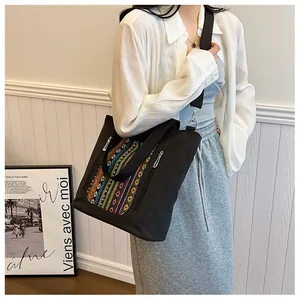 Detail of black canvas tote bag showing colorful ethnic embroidery pocket and zipper
