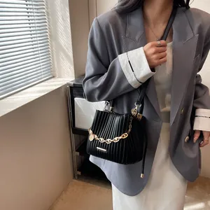Détail d'un sac seau plissé noir avec une grosse chaîne dorée et une plaque logo