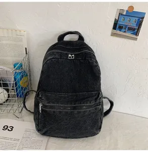 Dettaglio dello zaino in denim nero con cuciture bianche a contrasto e tasca frontale