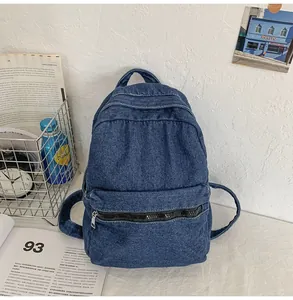 Dettaglio dello zaino in denim blu scuro con tasca a zip su una scrivania bianca pulita