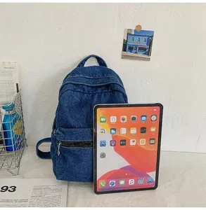 Dettaglio dello zaino in denim blu con manico superiore e tasca con zip con iPad per scala