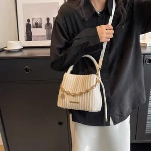 Détail du sac seau plissé blanc cassé avec chaîne dorée et plaque logo en métal