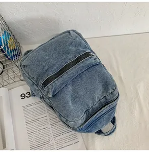 Dettaglio dello zaino in denim lavato blu con cerniera nera e trama della tasca frontale