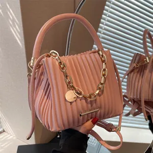Sac seau plissé rose avec chaîne dorée et bordure métallique, vue dans un miroir