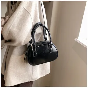 Gros plan d'un mini sac bowling noir brillant avec doubles poignées et détails zippés