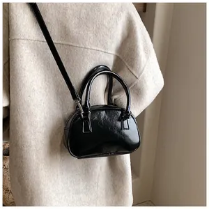 Détail d'un sac à main noir brillant avec ferrures argentées sur un manteau beige