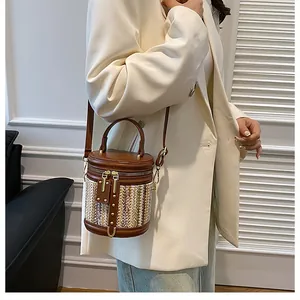 Detail of the brown cylinder straw bag with contrast leather stitching and gold hardware