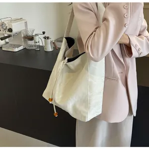 Detalle de bolso tote crema arrugado con cordón de cuentas de ámbar en café