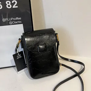 Detail of black mini crossbody phone bag with crinkle patent leather and gold hardware