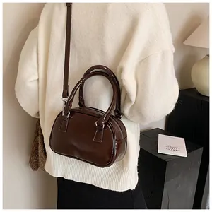 Vue détaillée du sac Boston en cuir marron foncé brillant avec poignées rondes et bandoulière
