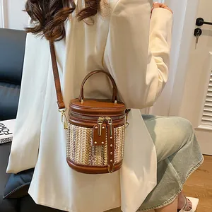 Chic two-tone cylindrical straw bucket bag with brown leather trim and gold studs