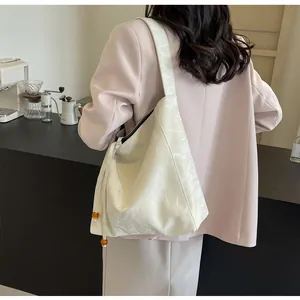 Detalle del bolso tote beige con textura arrugada brillante y cordón de cuentas de colores