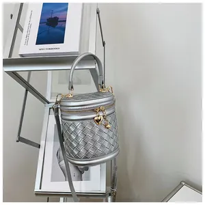 Détail d'un sac seau tressé argenté avec fermeture dorée et breloque en forme de cœur