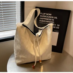 Detalle del bolso tote crema con cierre de cordón y elegantes cuentas de ámbar