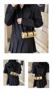 Close-up of golden cylinder pillow bag with black handles and metal texture finish