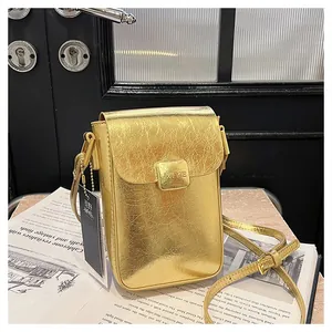 Detail of a gold metallic crossbody phone bag with crinkled texture on magazine background
