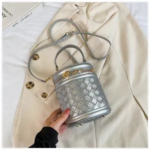 Détail du sac seau tissé argenté avec pendentif coeur sur un blazer beige
