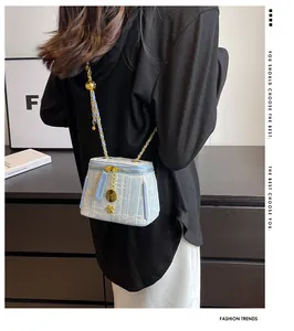 Close-up of light blue tweed crossbody bag with gold chain and round metal pendant detail