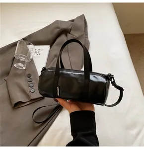 Close-up of black glossy cylindrical pillow bag with woven label and stylish shoulder strap