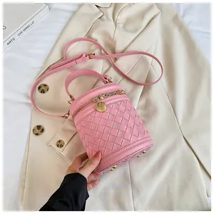 Détail d'un sac seau rose tressé avec pendentif cœur doré sur un blazer beige