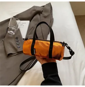 Detail of bright orange metallic cylinder bag with textured leather and black strap
