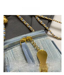 Detail of light blue tweed bucket bag with smooth golden zippers and camellia pendant