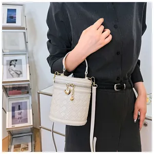 Détail d'un sac seau blanc tressé avec pendentif en cœur et bandoulière porté par un mannequin