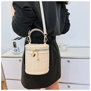 Détail du sac seau cylindrique tressé beige avec pendentif cœur et bandoulière réglable
