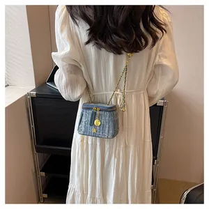 Detail of denim bucket bag with gold chain strap and floral charm on a white dress