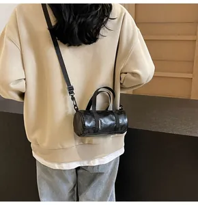 Rear view of a black glossy cylinder crossbody bag with adjustable wide strap on model