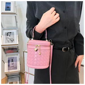 Détail d'un sac seau rose tressé avec pendentif coeur doré porté par un mannequin