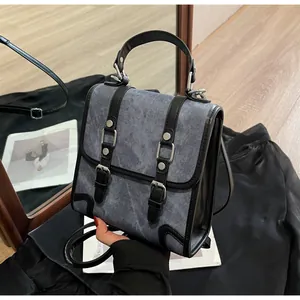 Detailed view of denim and black leather stitching with silver metal buckle on bag