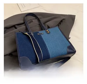 Detail of color-block denim handbag featuring contrast stitching and gold metal rivets
