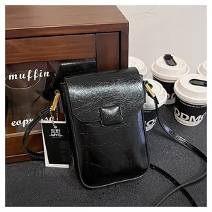 Close-up of black glossy wrinkled texture and brand buckle on stylish mini crossbody bag
