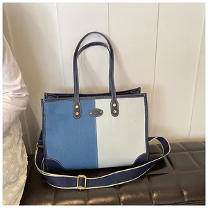 Detail of color-block denim tote bag with navy leather trim on a luxury leather stool