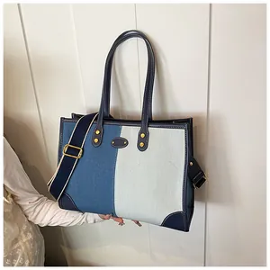 Detail of a large contrast denim tote bag with metal logo plate and adjustable strap