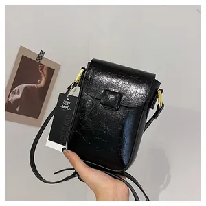 Detail of black glossy mini phone bag with wrinkled texture and golden hardware accents