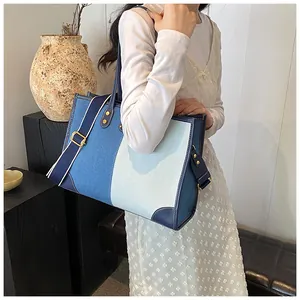 Detail of a large denim tote bag featuring blue color-block design and metallic rivets