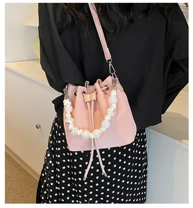 Pink drawstring bucket bag with pearl bead handle and slim shoulder strap on model