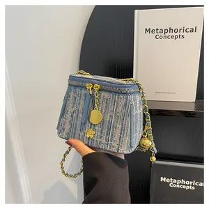 Mini tweed box bag in blue and grey with gold chain strap held by a person's hand