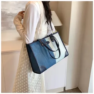 Detail of a large denim patchwork tote bag showing contrast stitching and leather handles