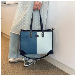 Detail of color-block denim tote bag with leather handles and gold rivet accents