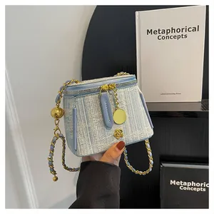Detail of light blue tweed bucket bag with gold chain strap and camellia metal charm