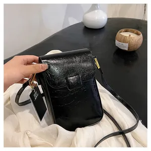 Detail of black mini crossbody bag featuring shiny patent leather with vintage crinkle texture