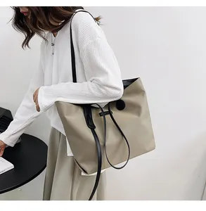 Detail of khaki nylon tote bag with black straps and brand patch on the surface