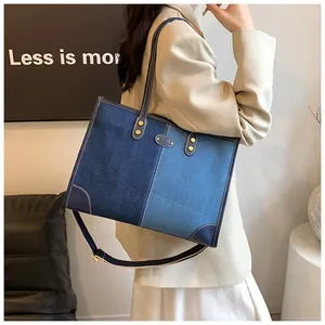 Detail view of denim tote bag showing color-block stitching and golden metal hardware