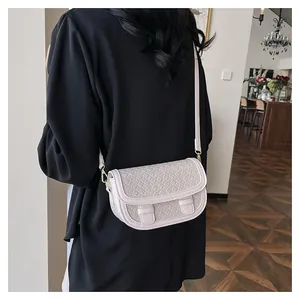 Detail of cream saddle bag featuring woven texture and decorative front buckles