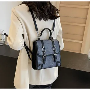 Rear view of a model wearing a grey retro British style backpack with silver hardware