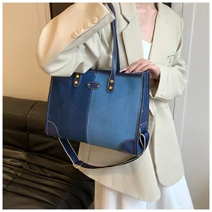Detail of color-block denim tote bag with leather trim and adjustable strap on a model